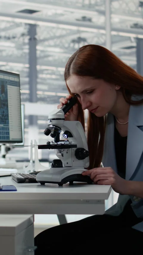 Woman in microelectronic facility studies microchip architecture with microscope Stock Footage 335882880