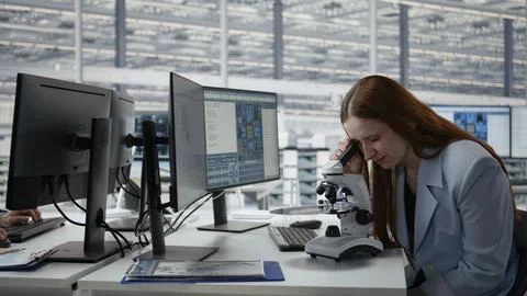 Woman in microelectronic facility studies microchip architecture with microscope Fotos de archivo