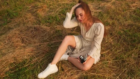 Woman, model sits in a field, posing for photographer at the camera for magazine Stock Footage 161529384