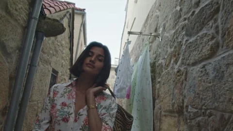 Woman models clothing while walking through a charming stone alleyway Stock Footage 320036033