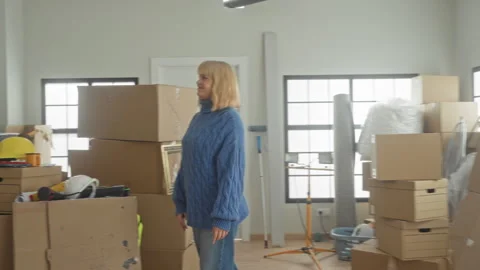 Woman with moving boxes resting hand on box in a cluttered apartment buildi.. Stock Footage 337386471