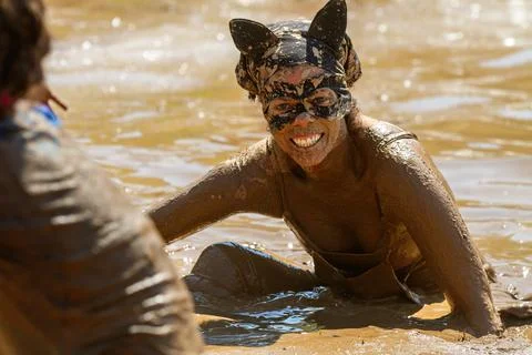 A woman is in a muddy pool wearing a cat mask and a black dress Stock Photos