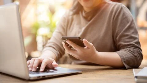 A woman multitasking, using her smartphone and laptop computer, working rem.. Stock Photos