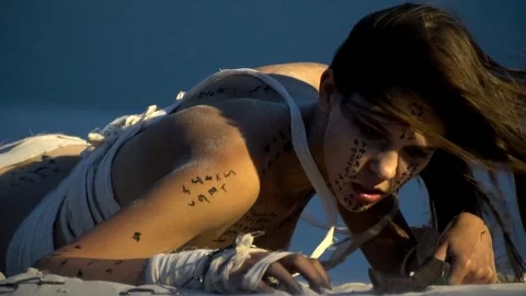 Woman mummy lies on the sand and looks at a black dagger in her hand Stock Footage