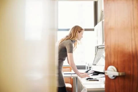 A woman in an office, seen through an open door. Stock Photos