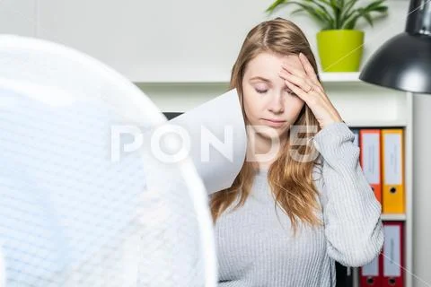 Woman in the office suffers from the heat and using a ventilator for cooling Stock Photos