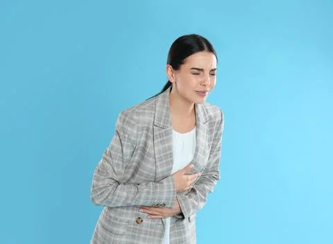 Woman in office suit suffering from stomach ache on light blue background Foo Stock Photos