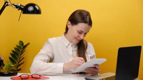 Woman office worker making notes with pen at notepad looking at laptop display Stock Footage 229884895