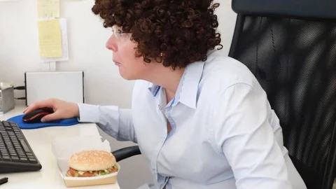 Woman at office on a workplace eats a hamburger Stock Footage 114610199
