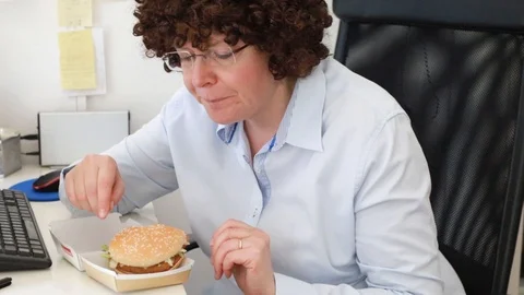 Woman at office on a workplace eats a hamburger Video stock 114610244