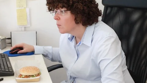 Woman at office on a workplace eats a hamburger Video stock 114610889