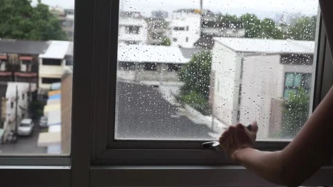 Woman opening window after rain, city houses background. Stock Footage