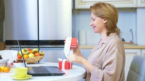 Woman opens a box with a gift while sitting at home in front of a laptop. Stock-Footage 145262850