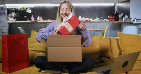Woman opens box pulling out birthday present in holiday wrapping Stockbeeldmateriaal 264477528