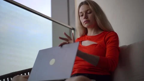 Woman opens laptop while sitting on the balcony by the sea Stock Footage 220644779
