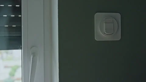 Woman operating wall control while external roller shutter goes up 스톡 동영상 332811506