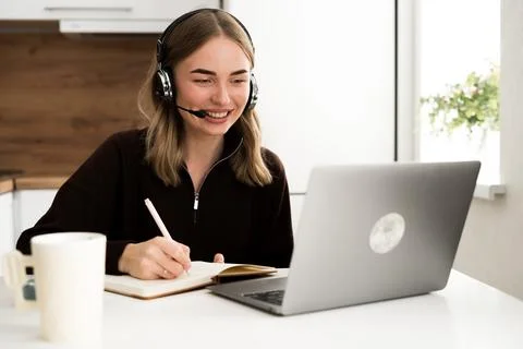 Woman operator with headset writing notes in notebook working remotely in t.. 스톡 사진
