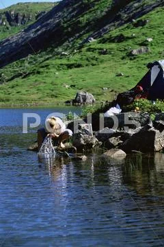 Woman outdoors at campsite washing face in lake Stock-Fotos