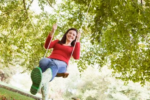 Woman outdoors on tree swing smiling (high key/selective focus) Stock Photos