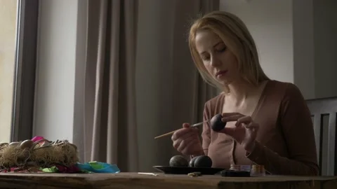 Woman paints Easter eggs while sitting at the table at home Video stock 146232221