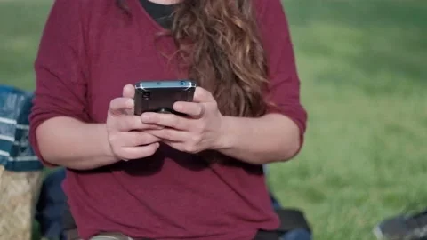 Woman In The park At Sunset And Uses Smartphone. Focus Of Mobile Phone Stock Footage