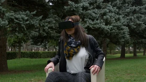 Woman in park using VR headset and smiling and looking at a pinecone Stock Footage 71469345