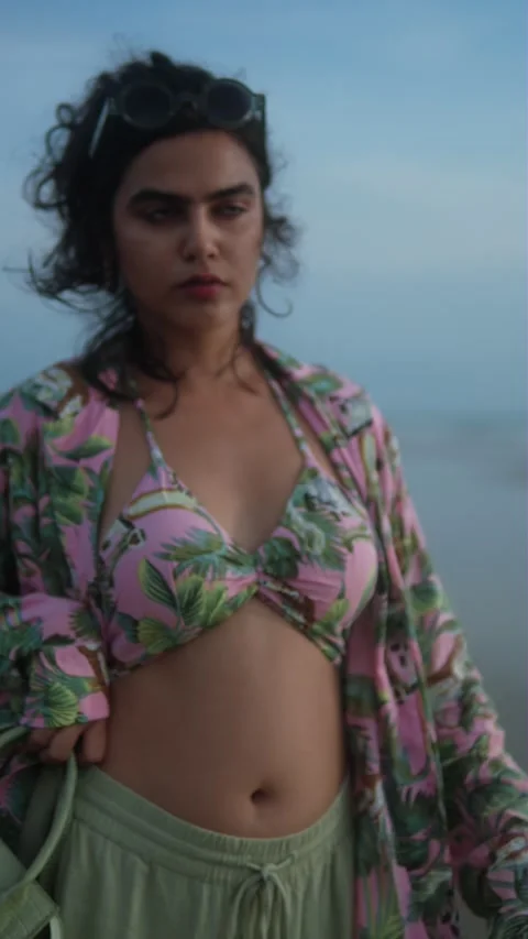 A woman in a patterned bikini stands on a beach at dusk with a calm, Video stock 292743608
