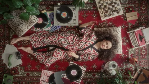 Woman in Patterned Robe Relaxing and Listening to Vinyl Music on Vintage Rug Stock Footage 339852384