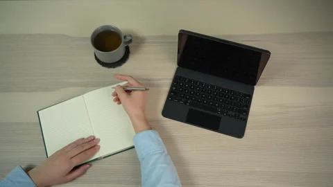 Woman pausing and thinking at workspace with notebook and laptop, top view Video stock 329010409
