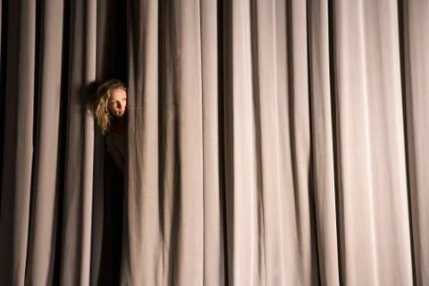 A woman peeking through a stage curtain Stock Photos