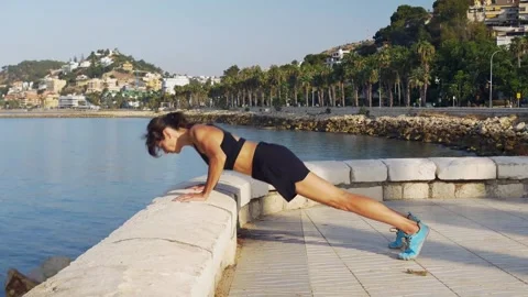 Woman performing controlled push-ups by the sea, demonstrating Stock Footage 345669300
