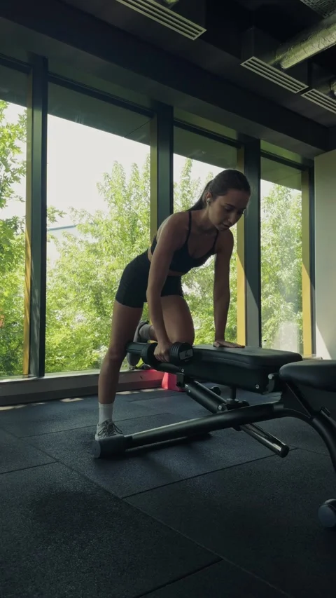 Woman performing a dumbbell row exercise on a bench at a modern gym 動画素材 339600335