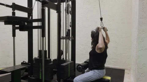 Woman performing lat pulldown on gym machine, strength workout Видео 325603825