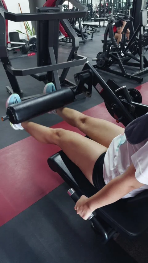 Woman performing leg extensions on a machine, focusing on her workout to develop Stock Footage 340959485