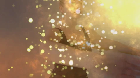 Woman performing prayer pose during yoga as golden sparkles swirl after light Stock Footage 313571005