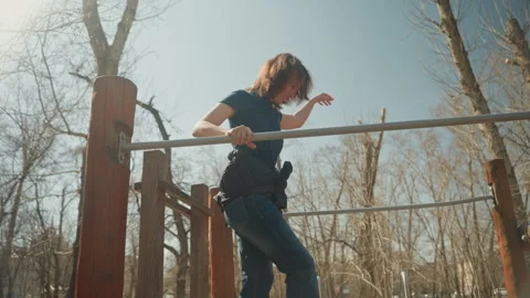 Woman performing pull ups on outdoor exercise bar with sunlight and bare trees Stock Footage 345046222
