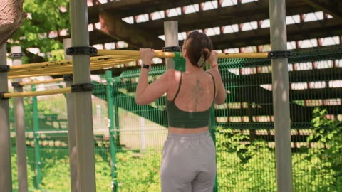 Woman performing pull ups on outdoor exercise bar with tattoos and wristwatch Stock Footage 345134821
