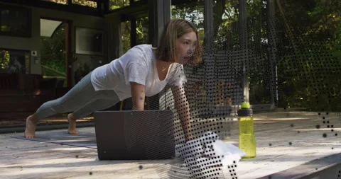 Woman performing push-ups on deck with mat and laptop as fitness tutorial 動画素材 318688996