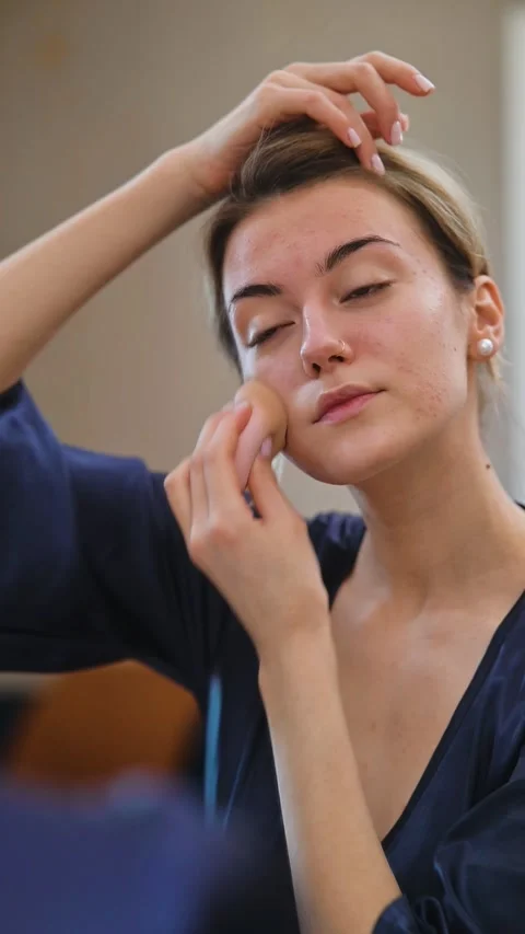 A woman performs her skincare routine by applying a facial product while looking Stock Footage 337555448