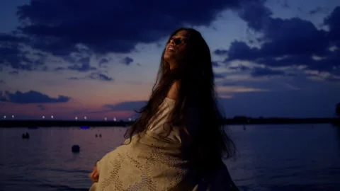 Woman performs a mystical dance performance under a dramatic twilight sky with Stock Footage 323331240