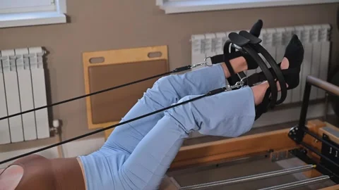 A woman performs a Pilates workout using a reformer machine in a fitness studio. Vidéo 344374834