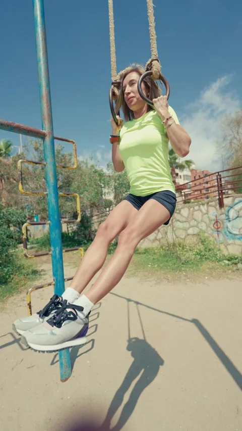 A woman performs pull-ups on monkey bars at an outdoor beach gym. The vertical Stock-Footage 304686113