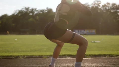 Woman performs squats using a resistance band on an outdoor track field during Stock Footage 286423808