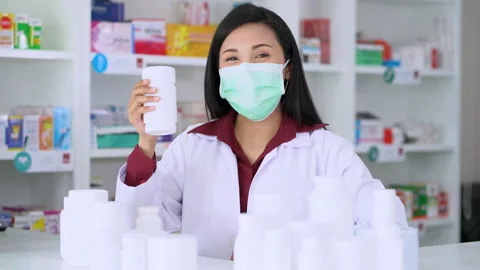 A woman pharmacist look a camera explaining each bottle of medicine in pharmacy Stock Footage 146106343