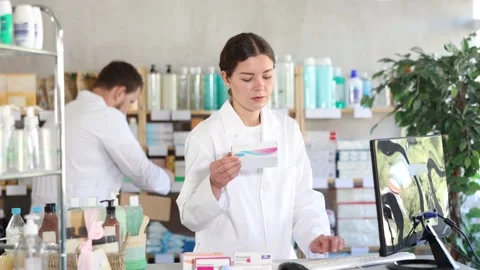 Woman pharmacist uses computer at workplace. Man assistant in background Stock Footage 327695253