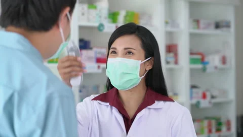 Woman pharmacist  wearing medical protective face mask using thermometer Stock Footage