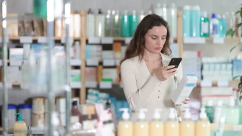 Woman in pharmacy scans QR code on cream product, studies item in detail Stock Footage 313458650