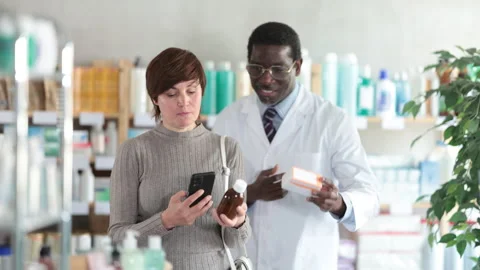 Woman in pharmacy scans QR code on antitussive syrup. African man pharmacist in Stock Footage 314244145