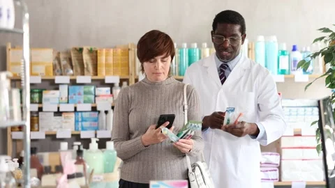 Woman in pharmacy scans QR code on toothbrush. African pharmacist in background Stock Footage 317986432