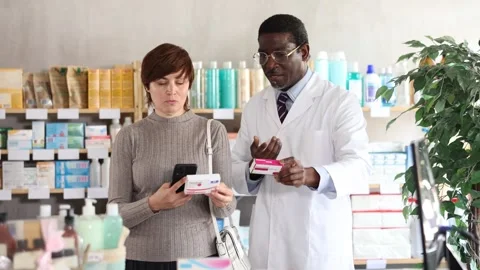 Woman in pharmacy scans QR code on paracetamol pills. African man pharmacist in Stock Footage 319486416